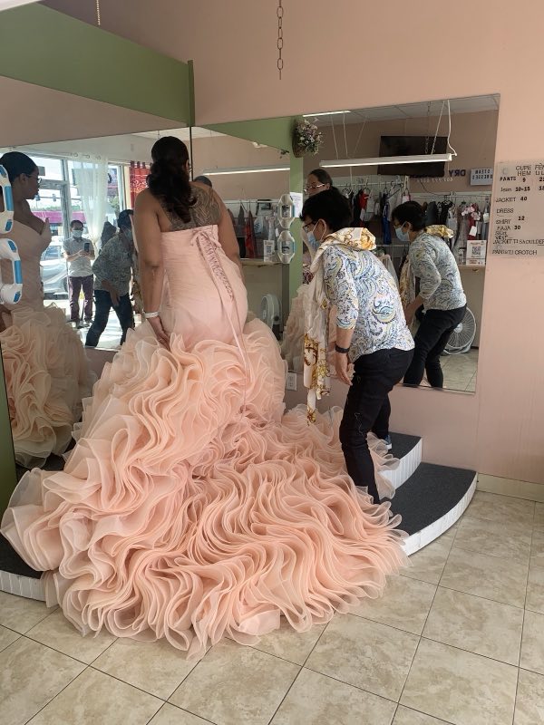 The tailor adjusting a blush ruffled ball gown on the shop's fitting platform