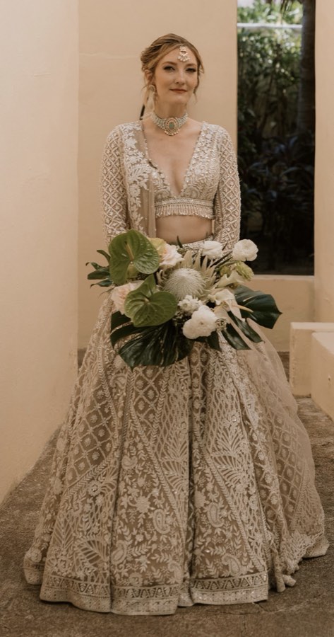 Client in an ornate cream and gold lehenga holding a bridal bouquet