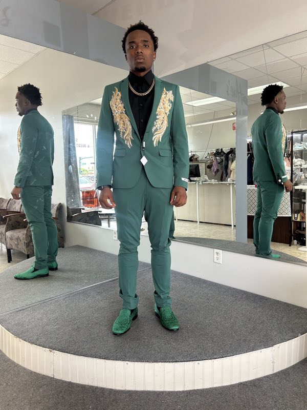 Client in a tailored green suit with gold lapel embroidery in front of the shop mirrors